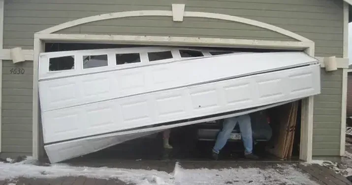 A man is standing in a garage with a broken garage door.