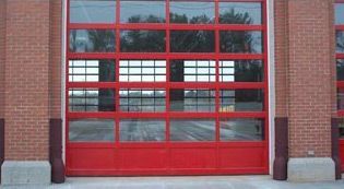 A red garage door with a lot of windows on a brick building.