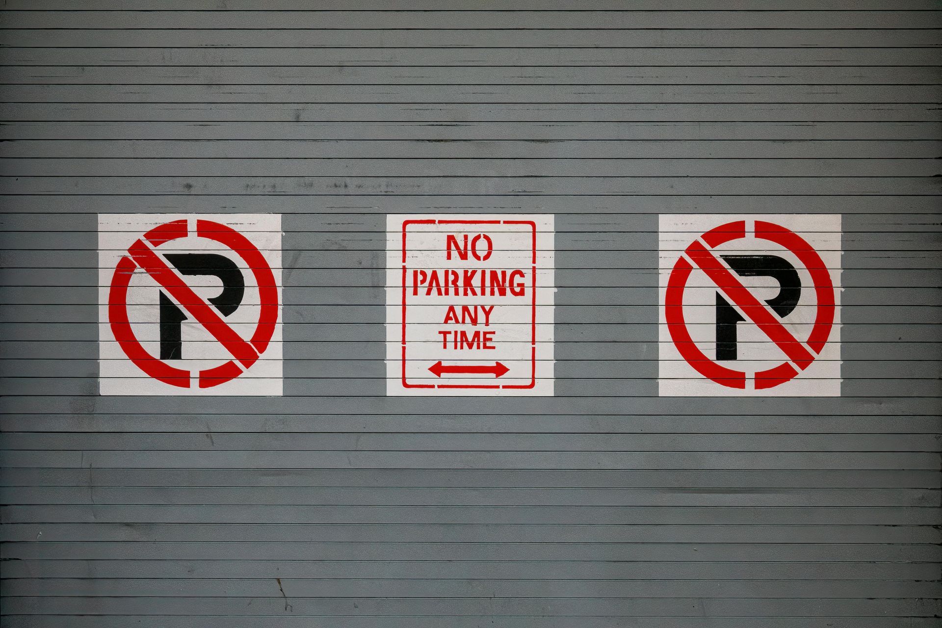 Three no parking signs are painted on a garage door