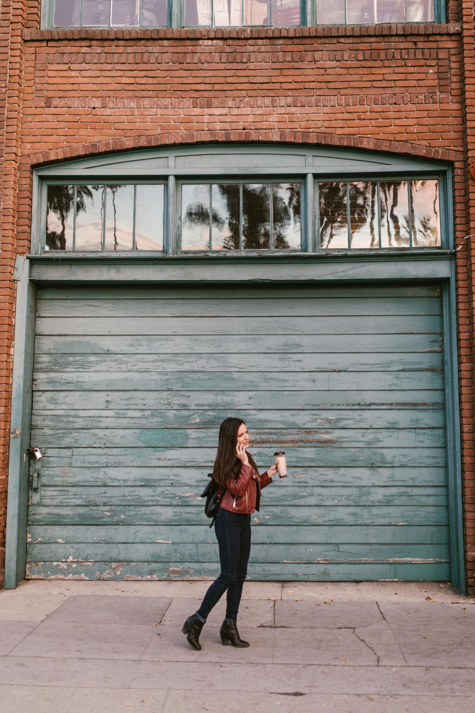A woman is walking down the street in front of a blue garage door.