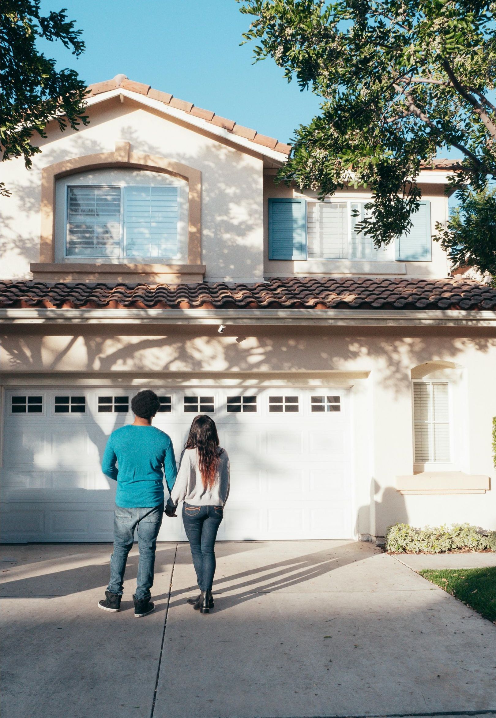 A man and a woman are standing in front of a house holding hands.