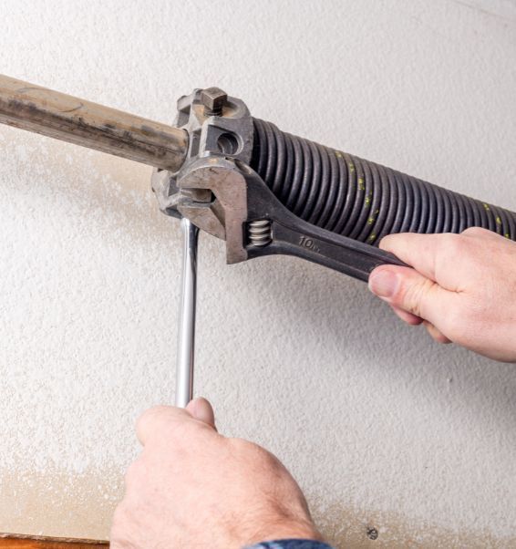 A person is fixing a garage door spring with a wrench and screwdriver.