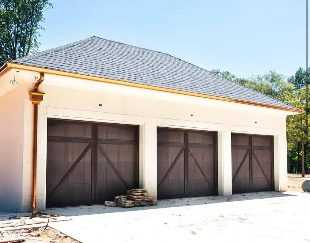A garage with three brown garage doors and a copper gutter