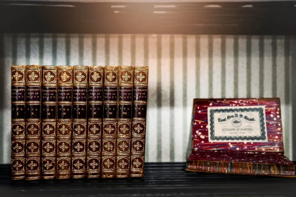Two ornate vintage chairs with green velvet upholstery face each other across a small table, set against yellow wallpaper.