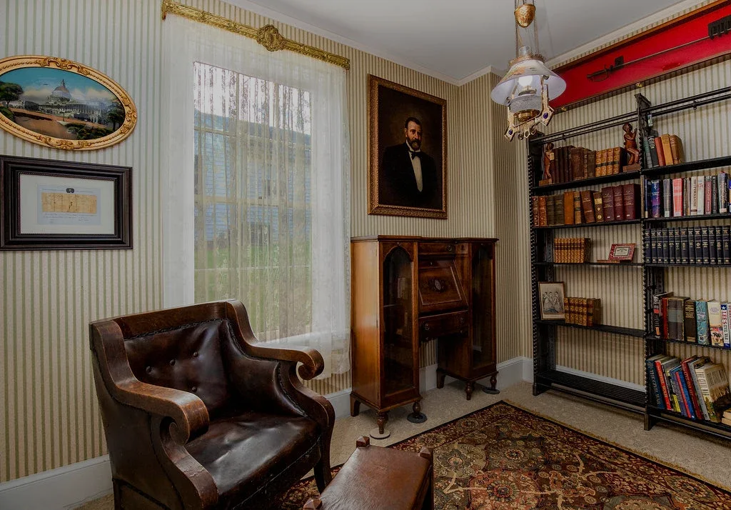 A vintage study featuring a leather armchair, a wooden secretary desk, a large bookcase, and framed art on striped walls.