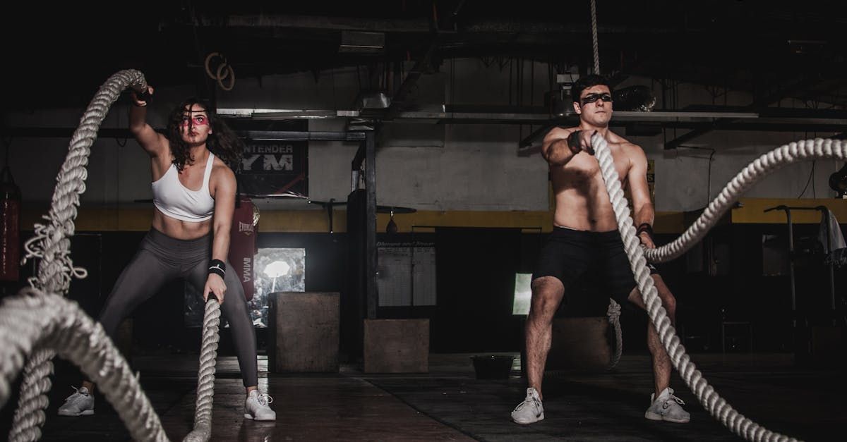 A man and a woman are holding ropes in a gym while personal training.