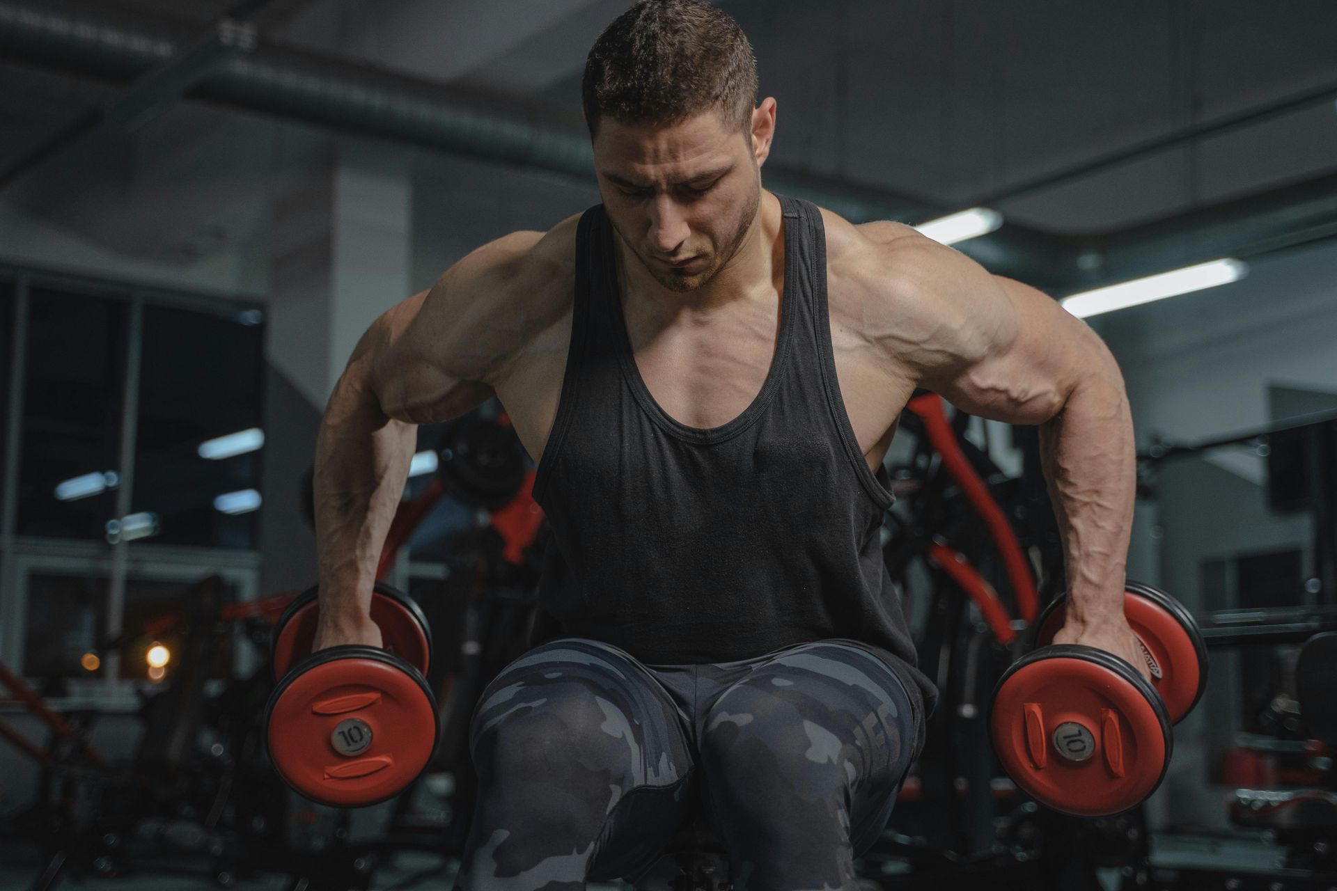 A man is sitting on a bench holding dumbbells in a gym.