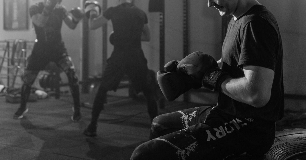 A black and white photo of a man wearing boxing gloves in a gym.