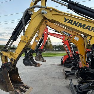 A row of excavators are parked next to each other in a parking lot.