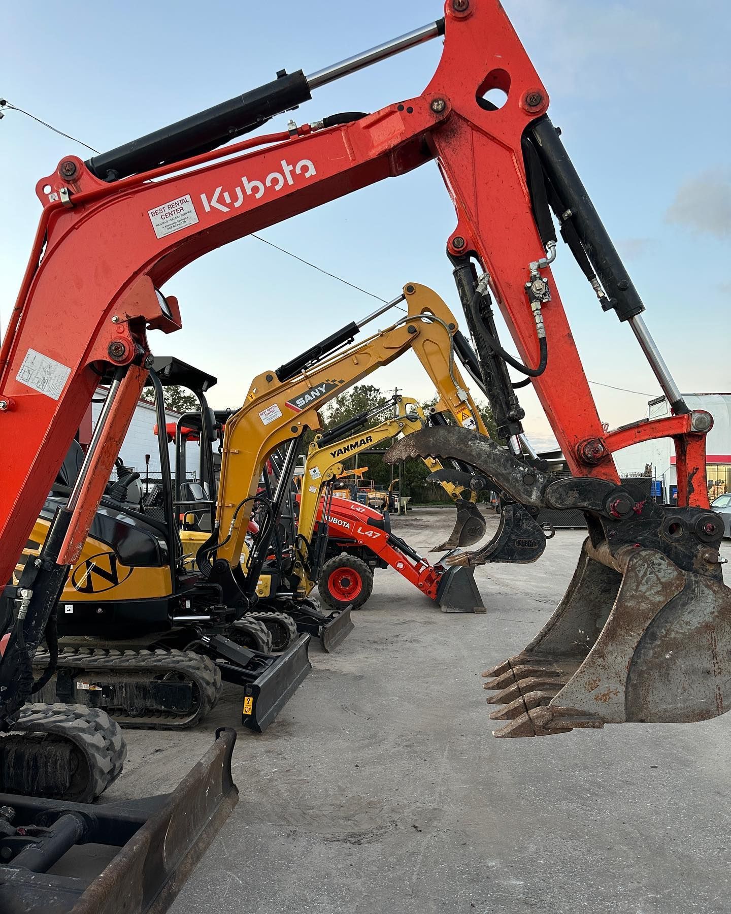 A row of excavators are parked in a lot.