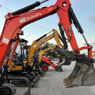 A row of construction vehicles are parked in a lot.