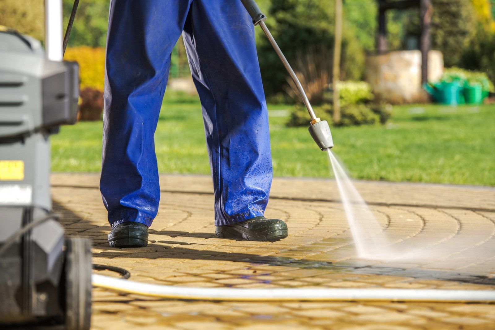 A man is using a high pressure washer to clean a brick walkway.