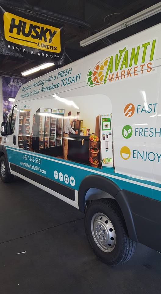 A white Avanti Markets delivery van is parked indoors, featuring brand logos, contact details, and a virtual market display.
