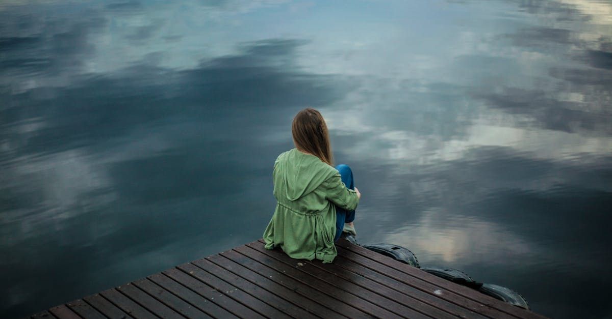 A woman is sitting on a dock looking at the water.