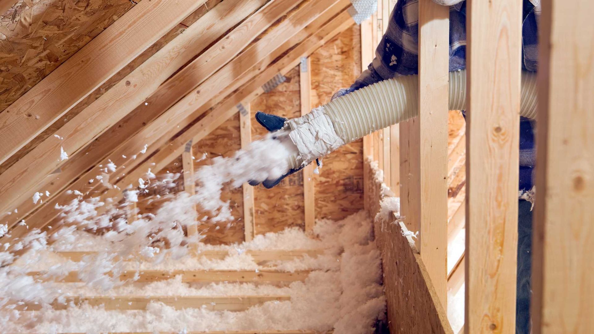 A person is blowing insulation into the attic of a house.