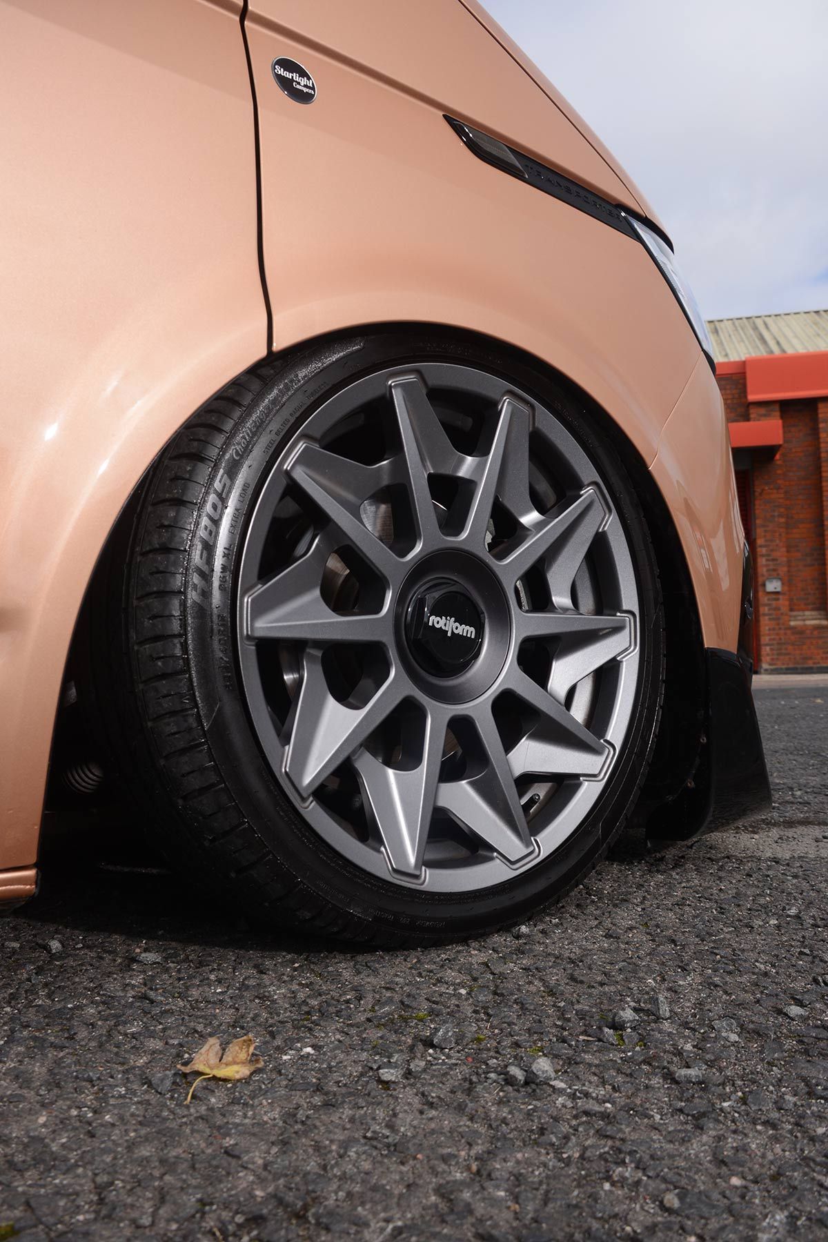 Close-up of a peach car’s front wheel with gray alloy rim on wet pavement