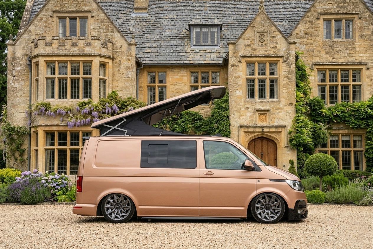 Tan van with pop-up roof parked before a stone manor house and gardens