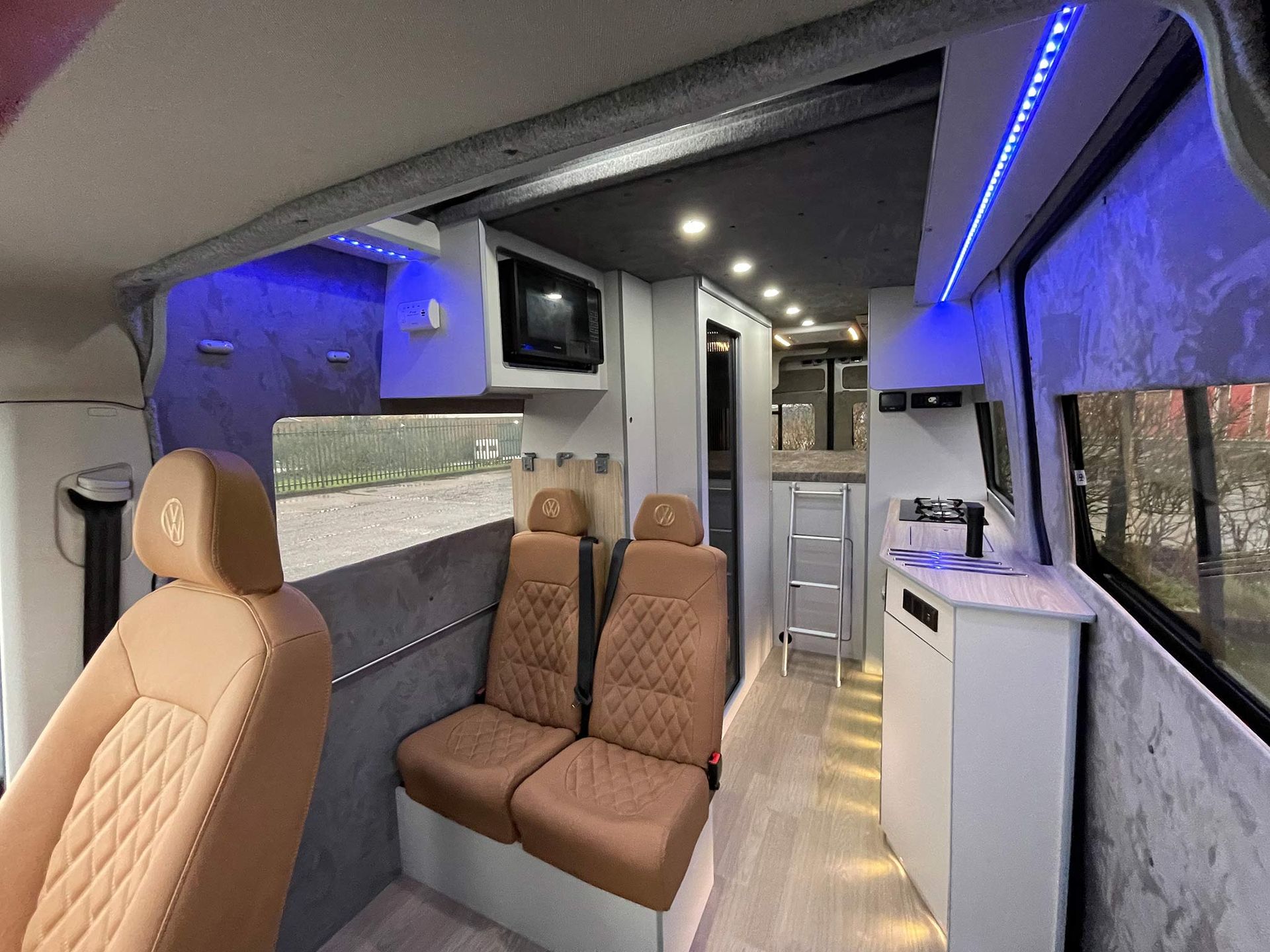 Modern van interior with tan quilted seats, blue LED lighting, and a compact kitchenette on the right