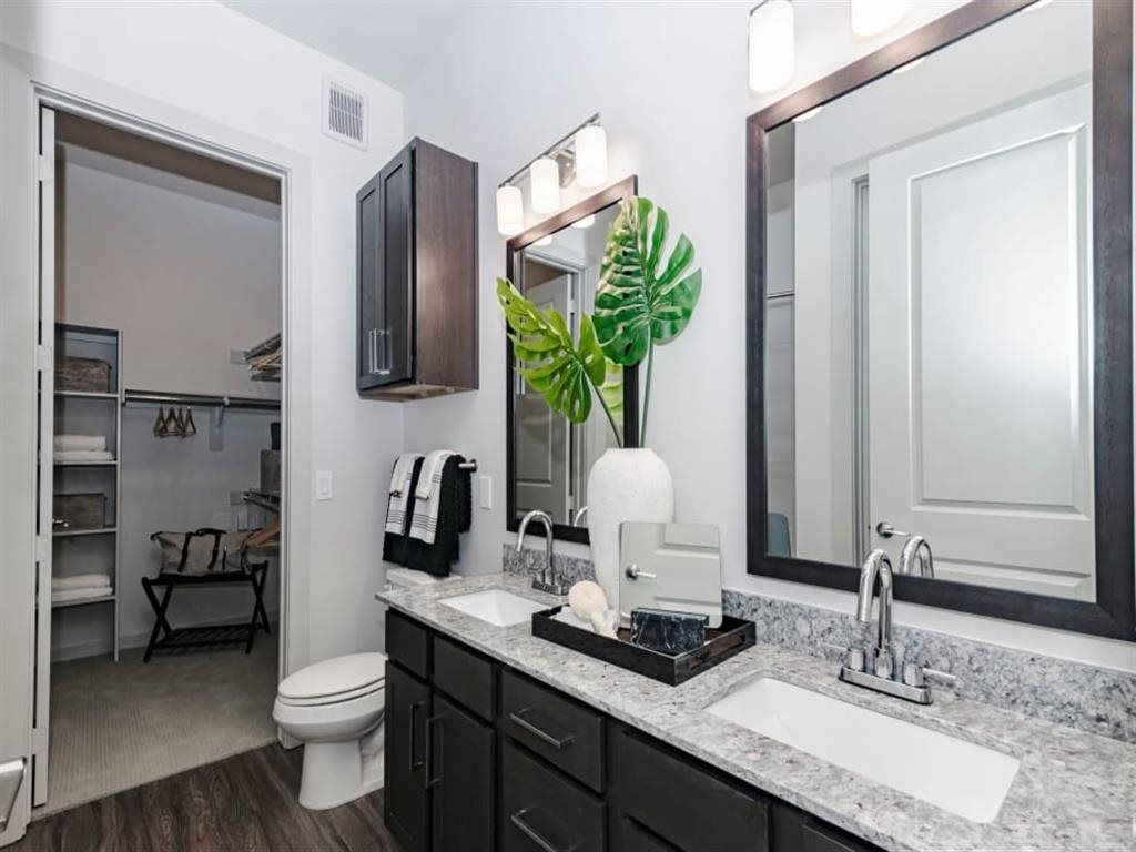 A bathroom with two sinks , a toilet , and two mirrors.