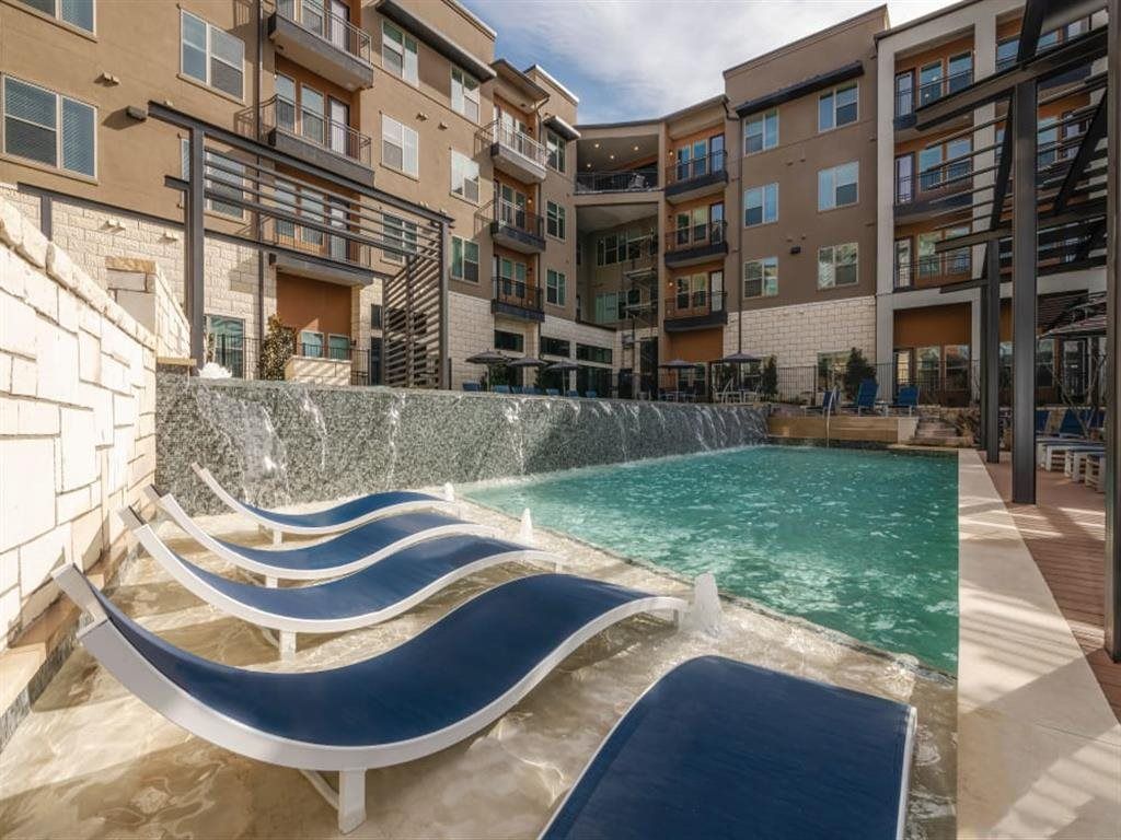 A swimming pool with a waterfall and lounge chairs in front of a building.