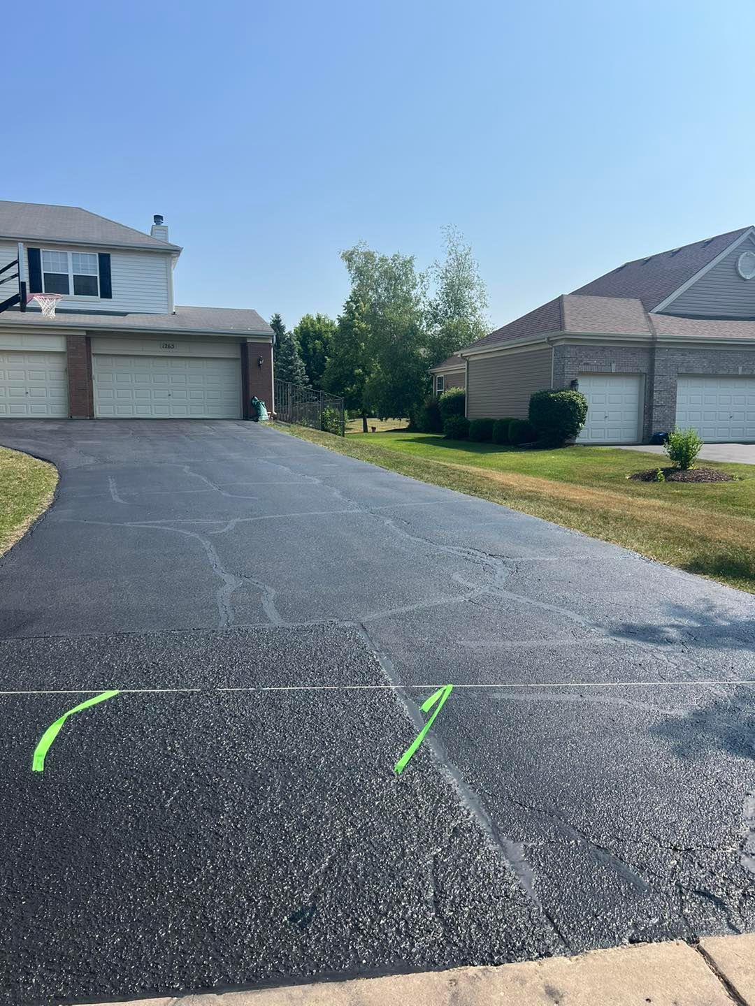 Driveway with fresh black asphalt and green marking paint between two suburban houses on a sunny day