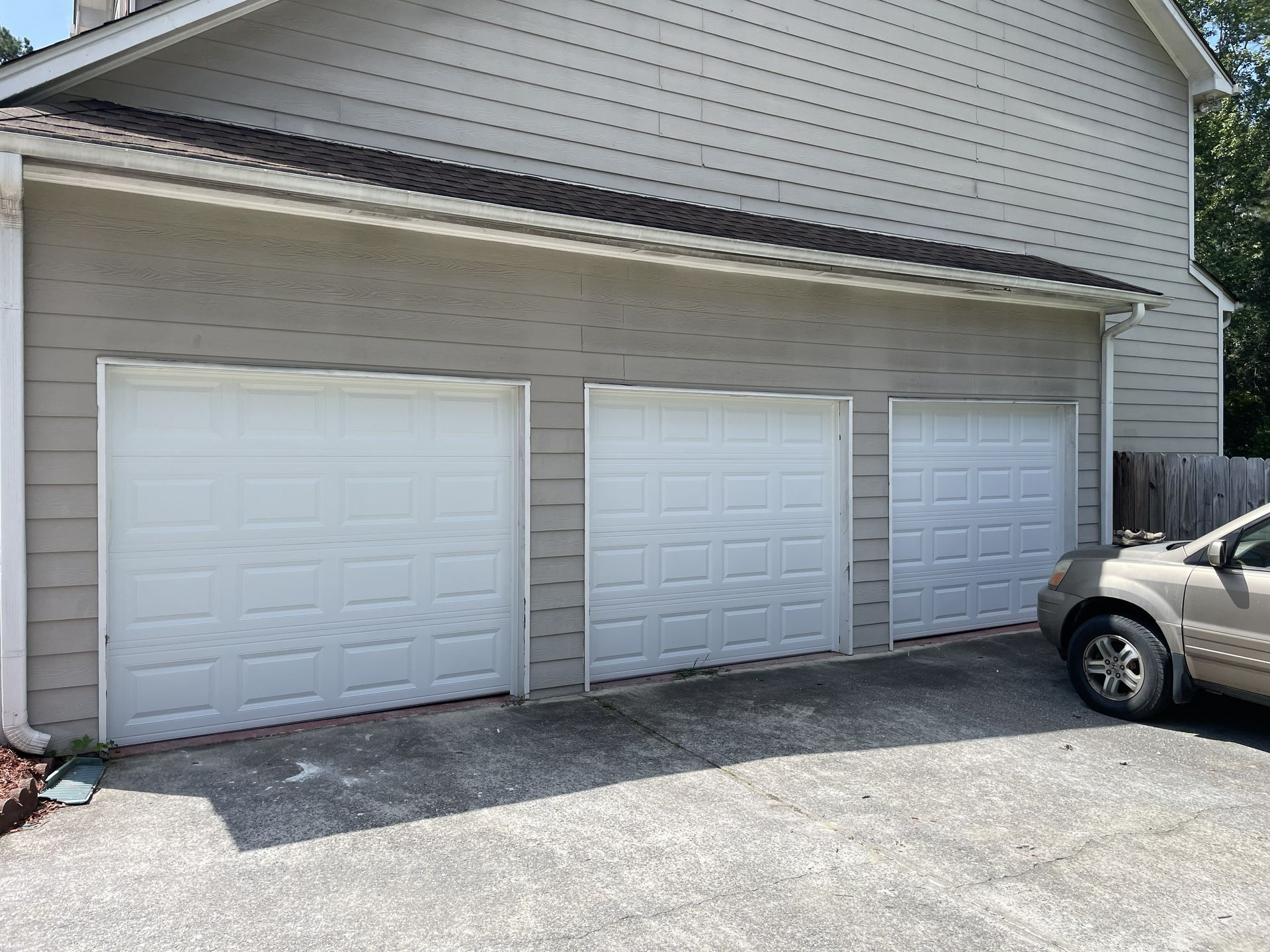 Three white garage doors on a light gray house. A car is parked on the driveway.