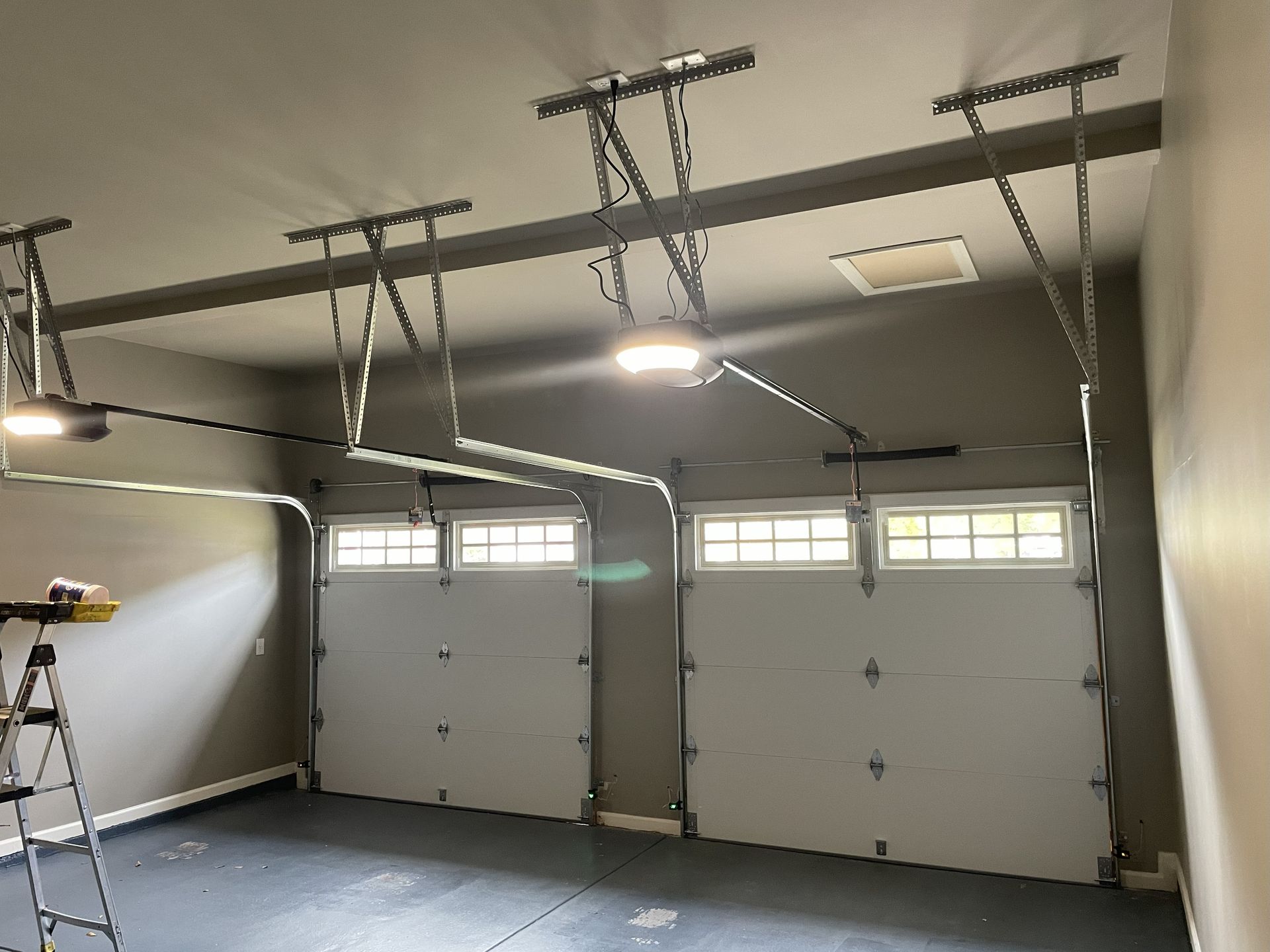Two closed garage doors with openers visible, inside a garage with grey walls and ceiling.