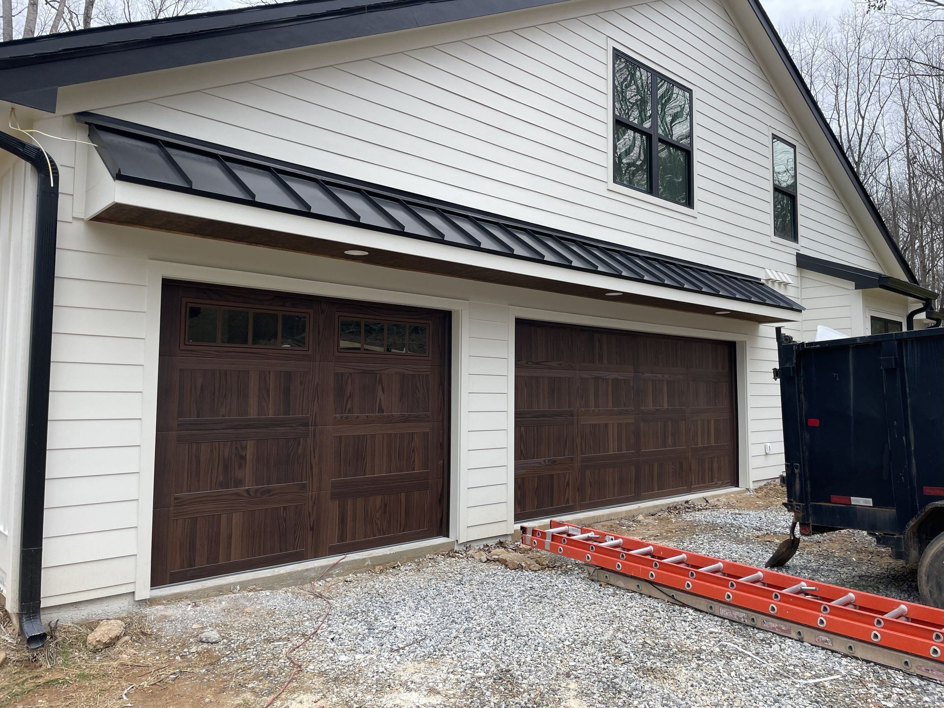 White house with two brown garage doors and a black roof.