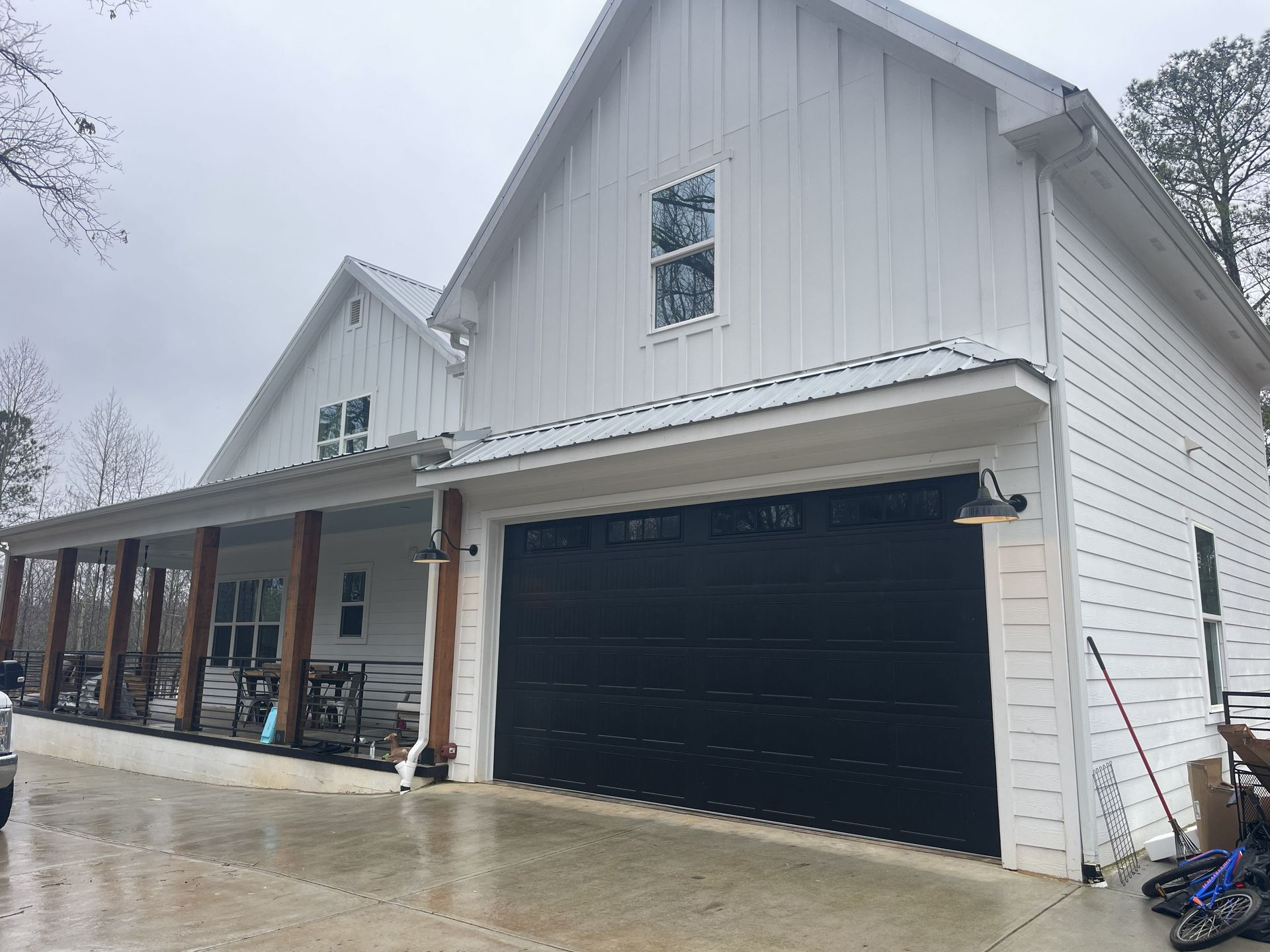 White farmhouse with black garage door, covered porch, and metal roof.