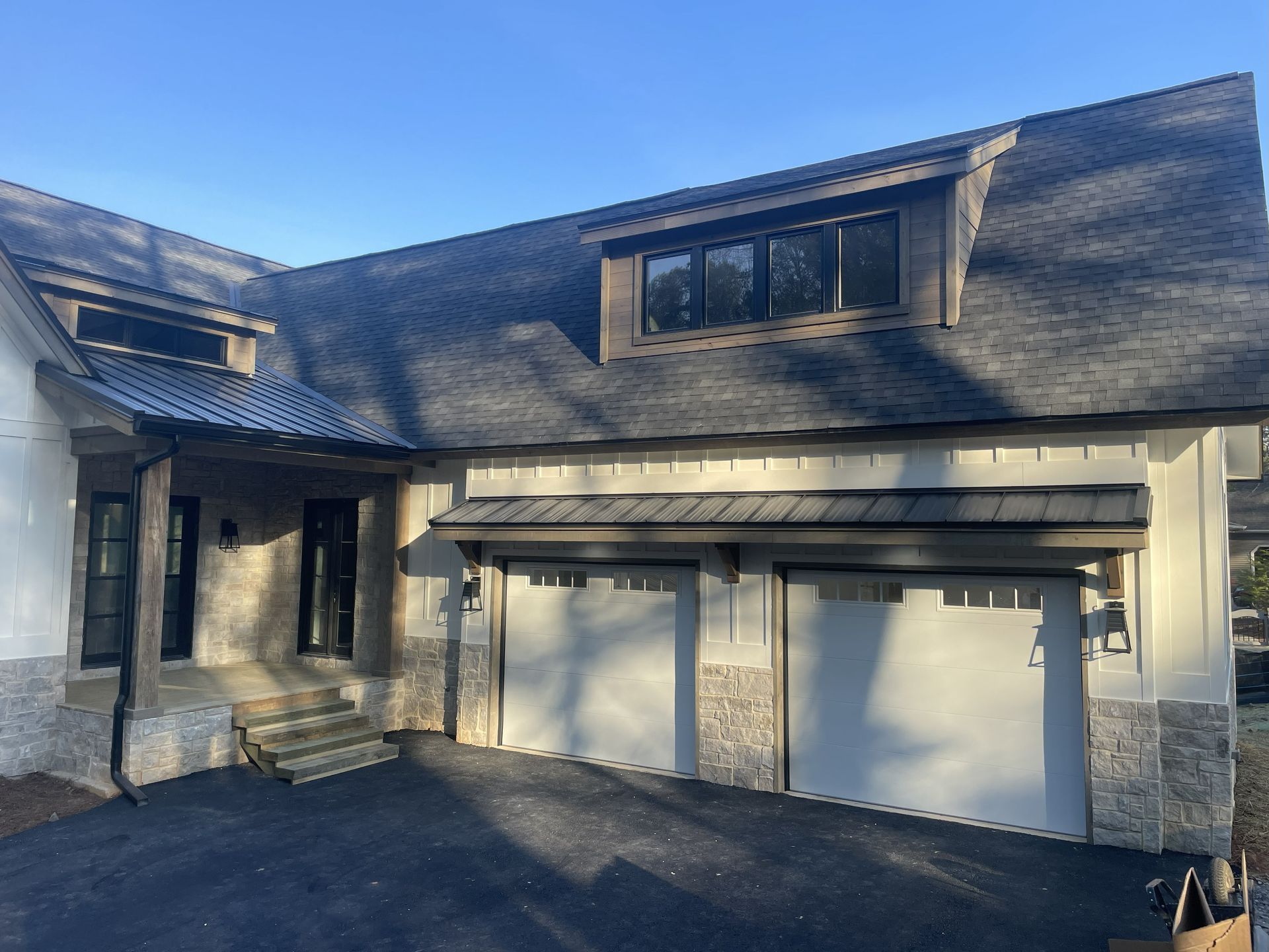 Exterior view of a house with garage doors and stone accents, under a dark roof.