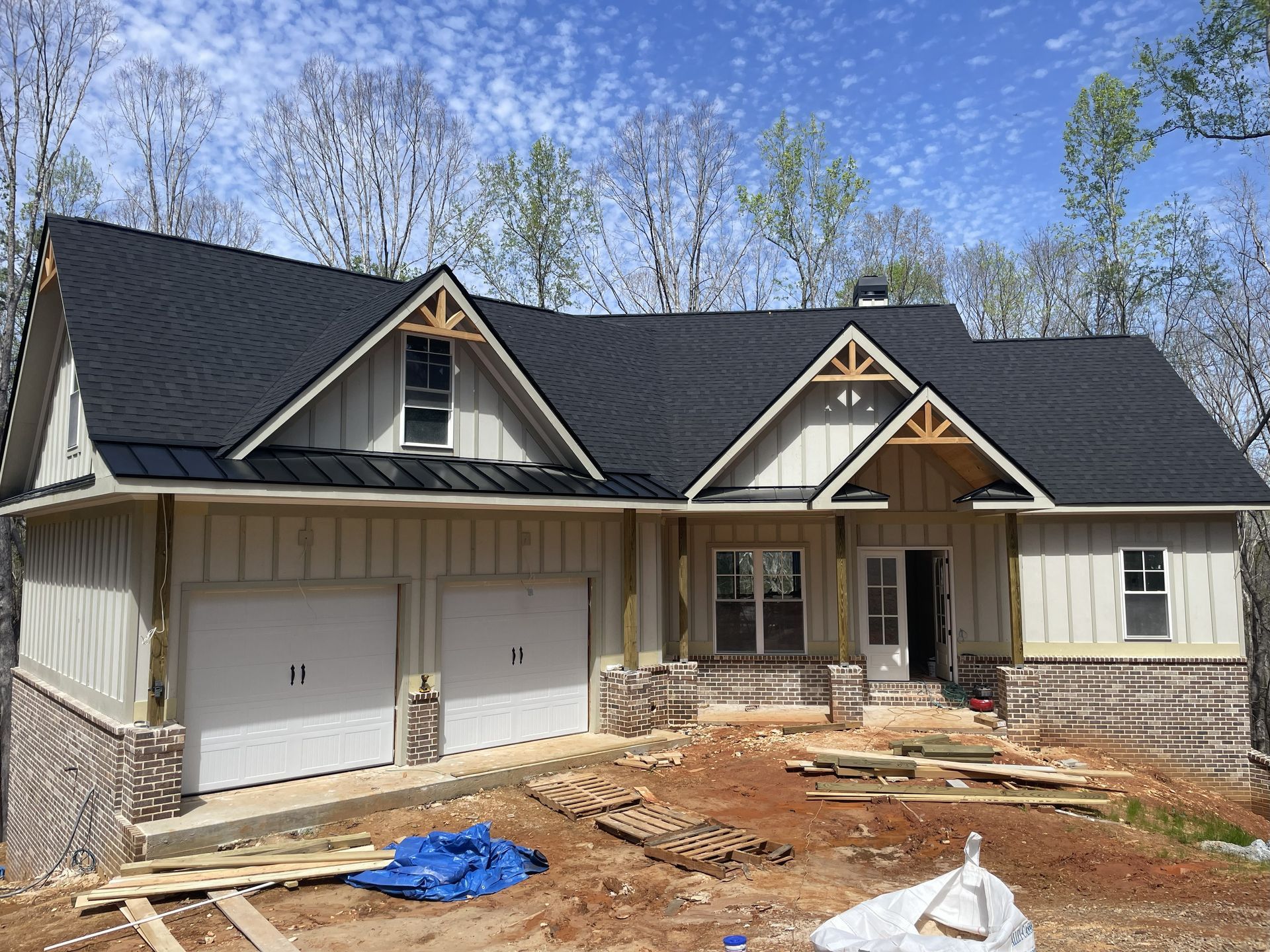 New house under construction with a black roof, tan siding, and a brick foundation.