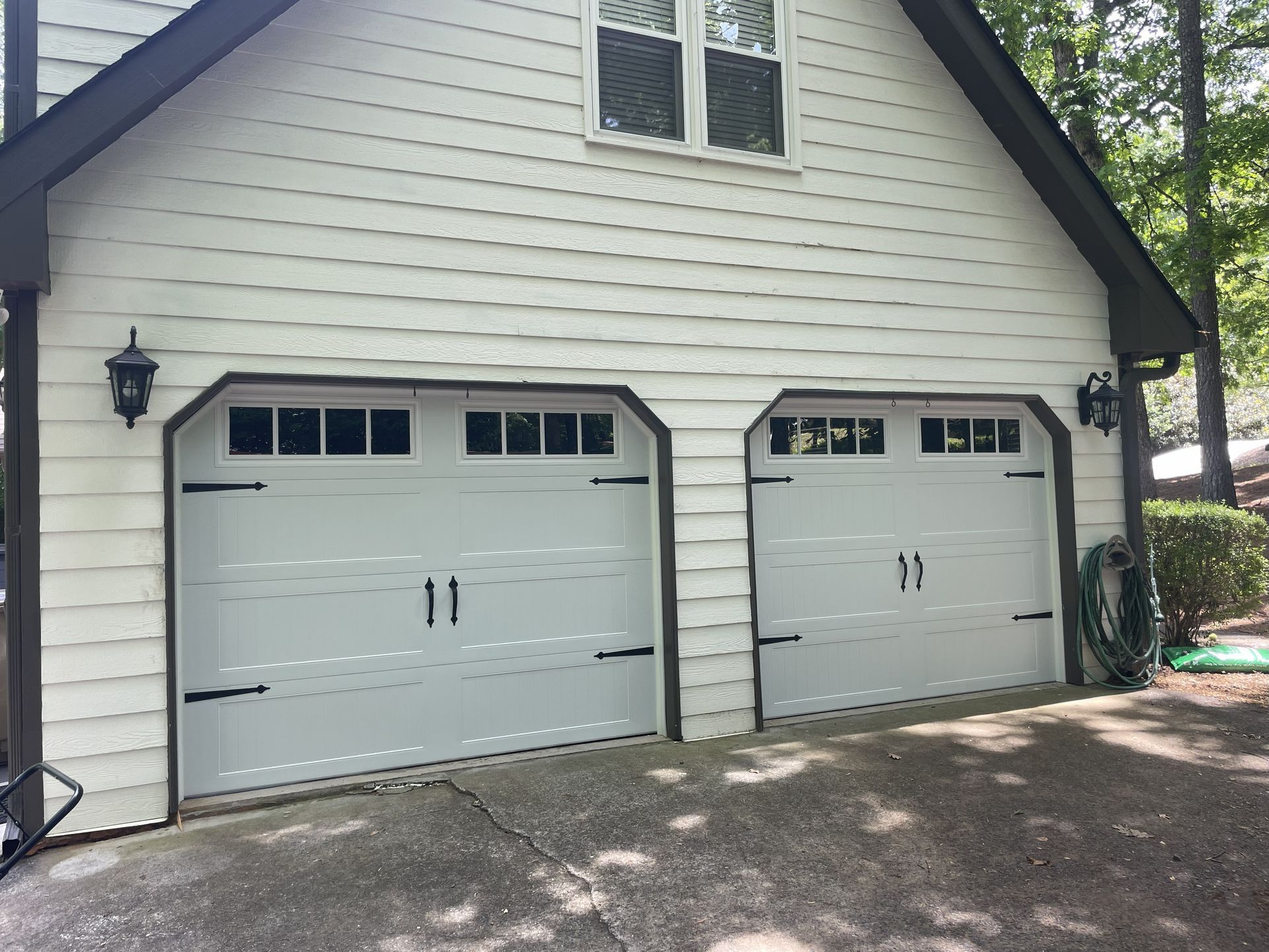 White garage doors with black accents, surrounded by white siding and brown trim.