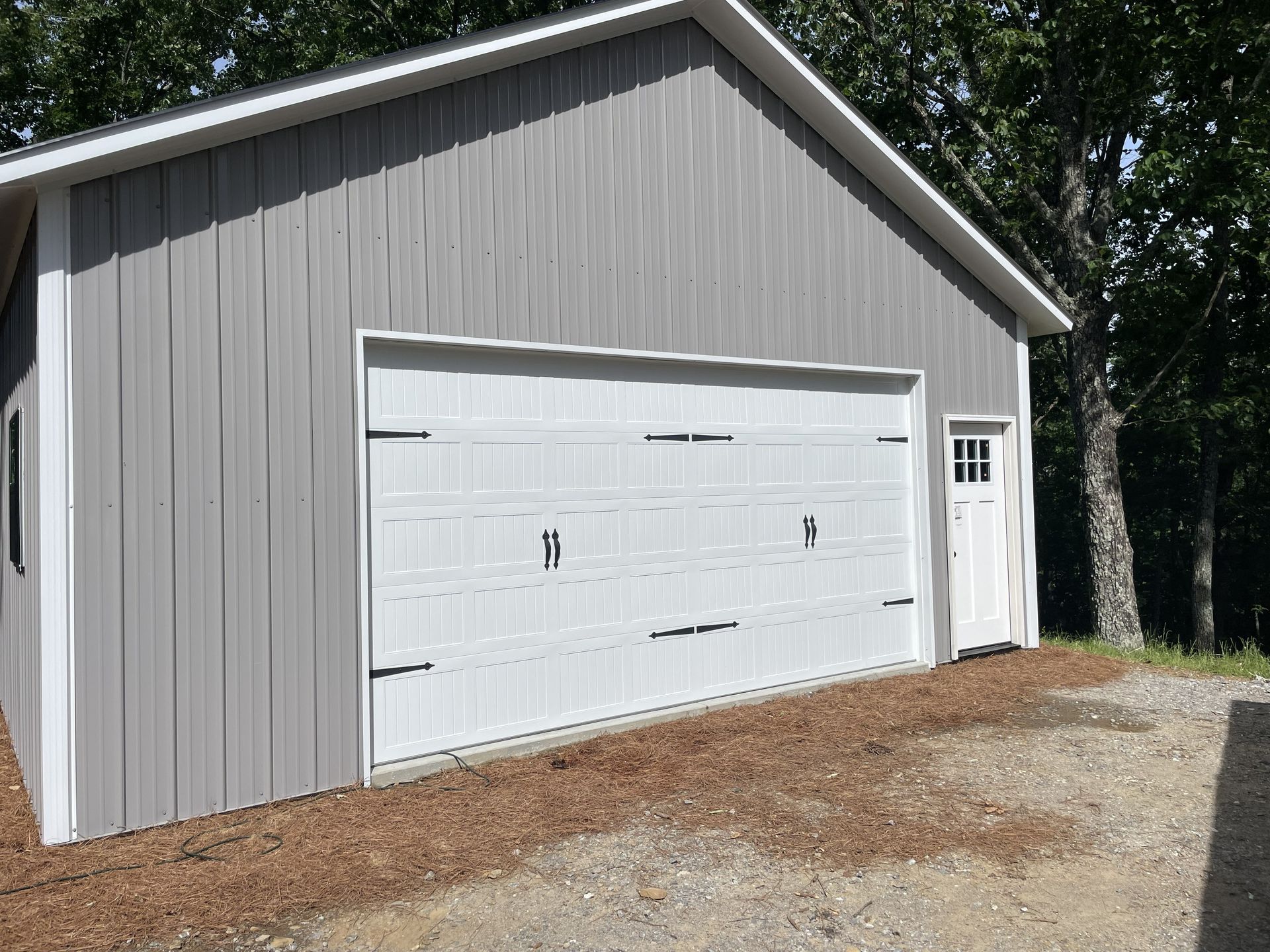 Gray garage with white garage door and small side door on gravel surface.