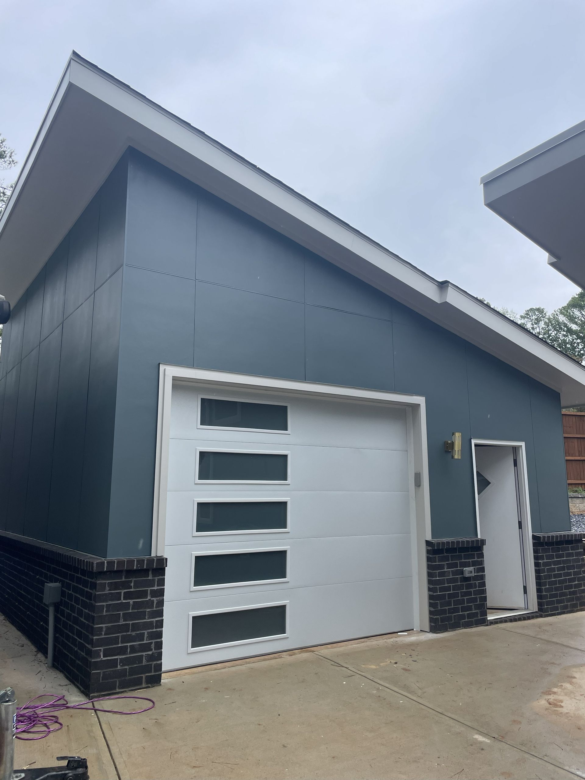 Modern garage with a white garage door, dark blue siding, and black brick accents.