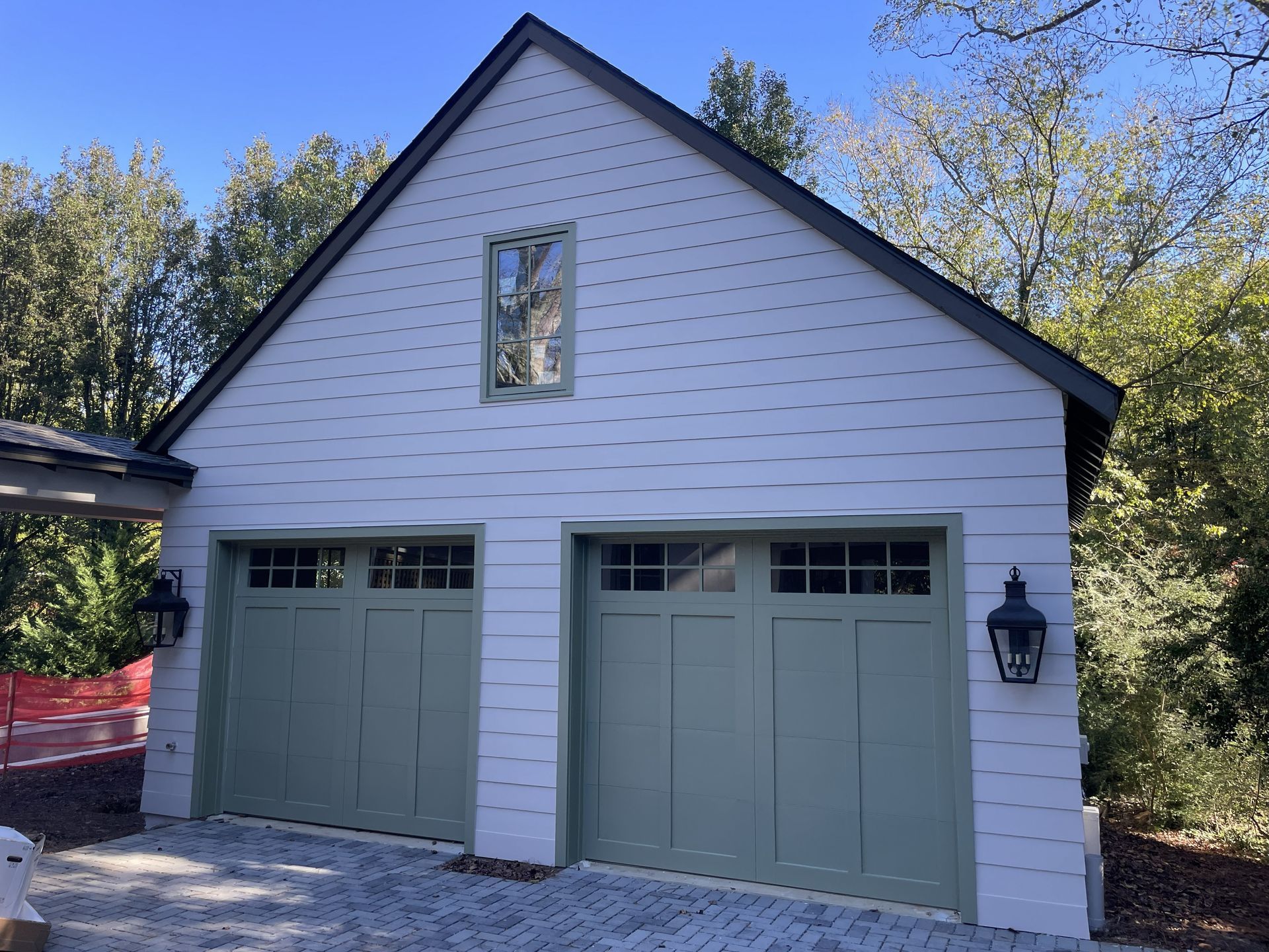 Two-car garage with green doors, white siding, and a small window under the dark roof. Lanterns flank the doors.