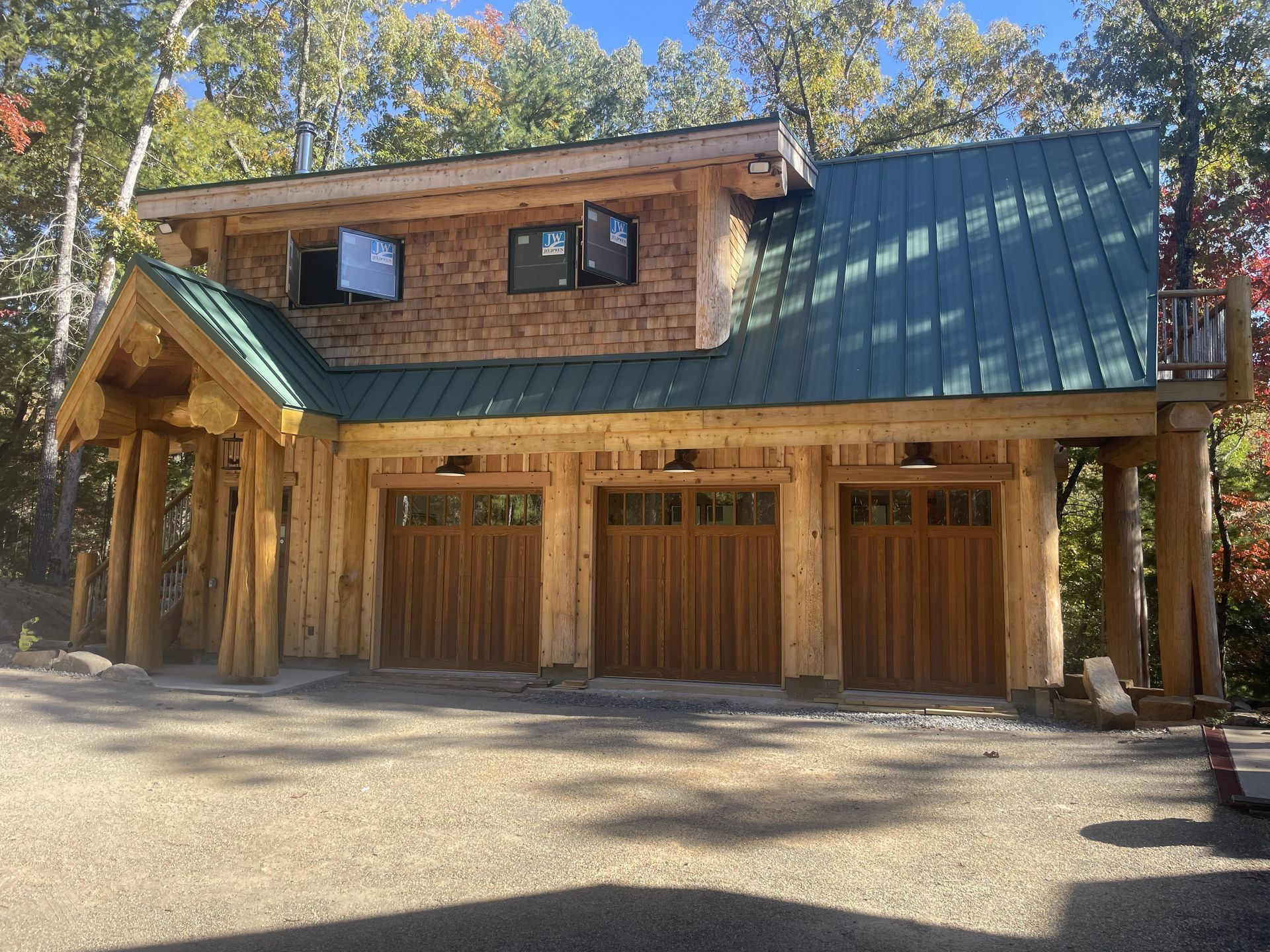 Wooden garage with three bays, green roof, and upstairs living area, set in a wooded area.