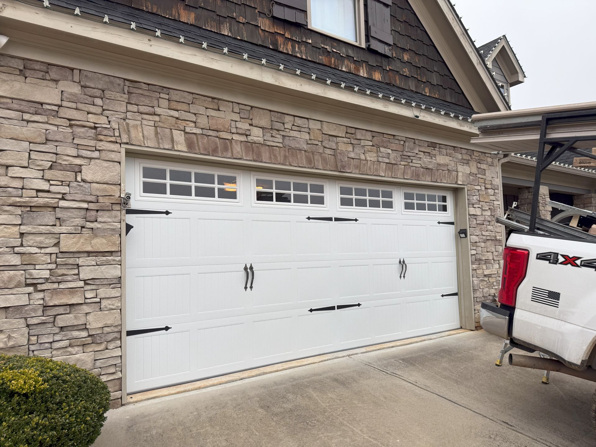 White garage door with decorative hardware, set in a stone facade. A truck is parked nearby.