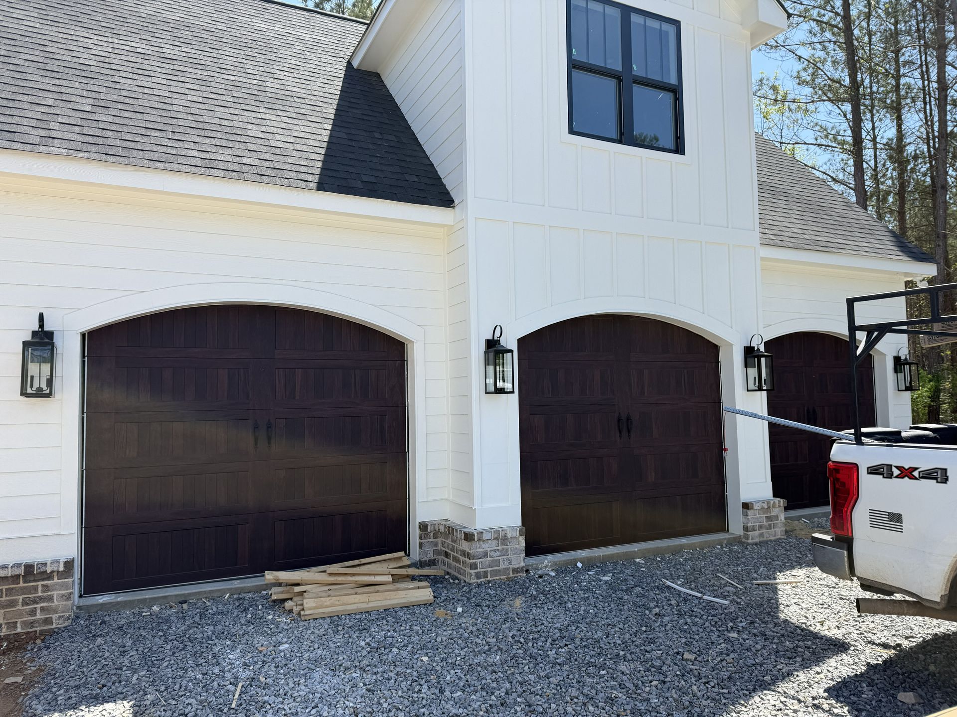 White house with brown garage doors and gravel driveway.