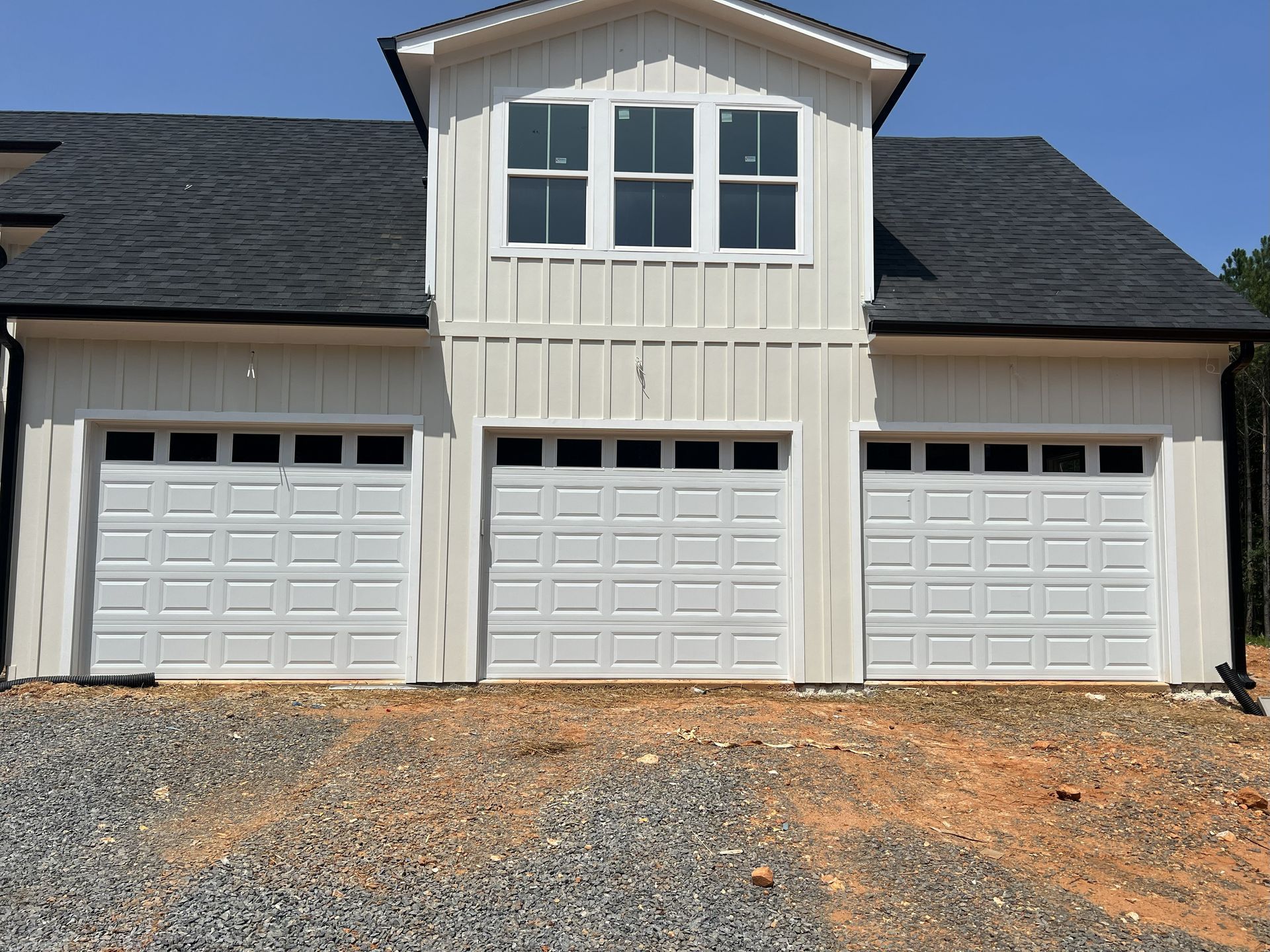 White three-car garage with a gabled loft and three windows under a dark roof.