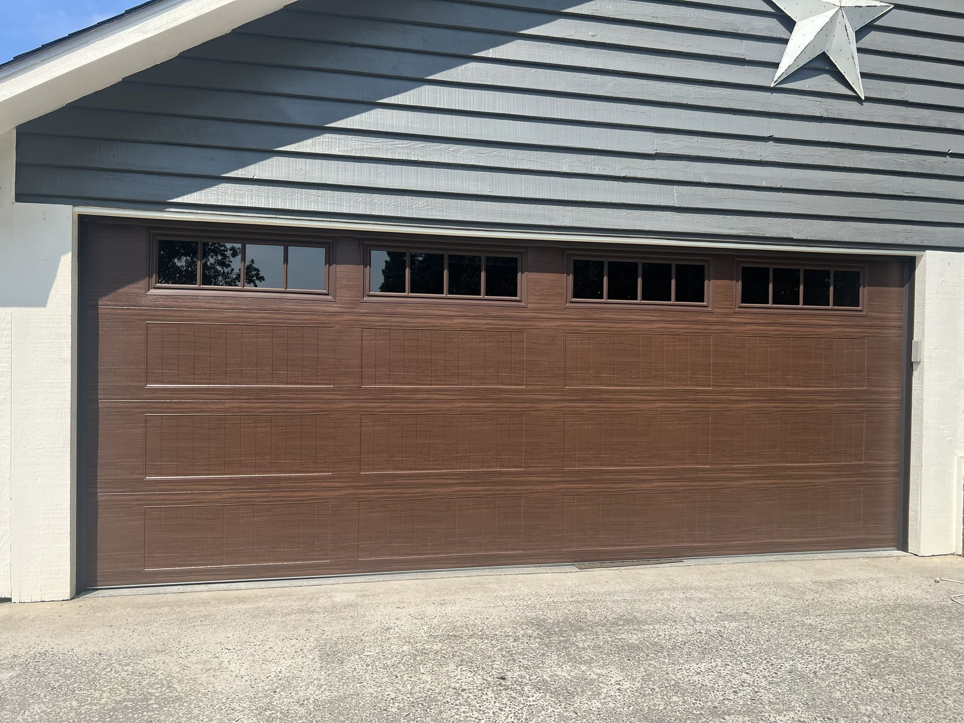 Brown garage door with windows, under blue siding, star above.