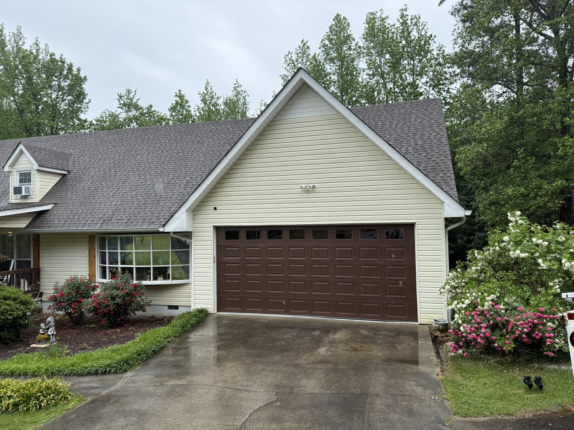 Brown garage door on a beige house with a gray roof; trees in the background.