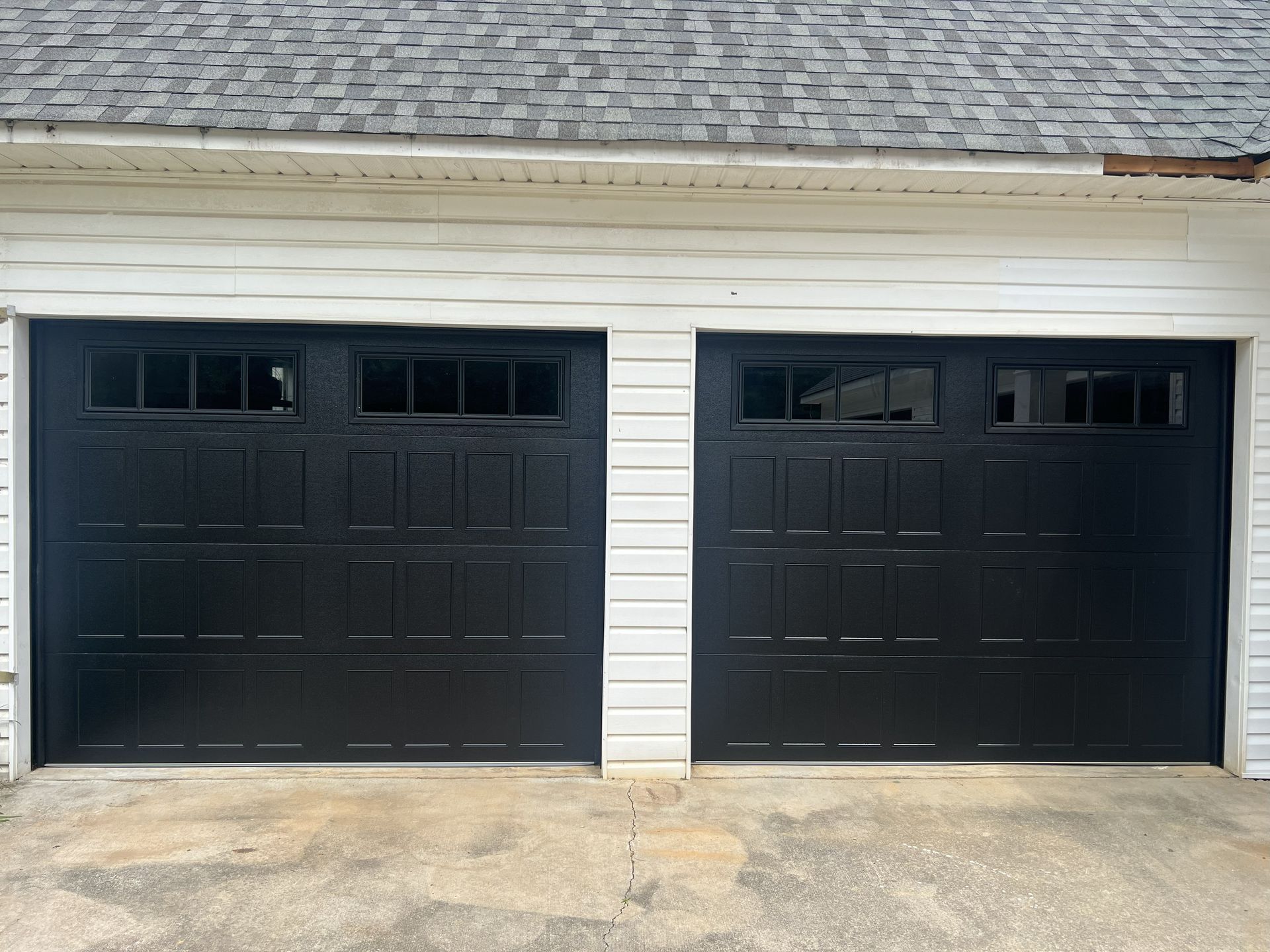 Two black garage doors with window panels. White trim, gray roof.