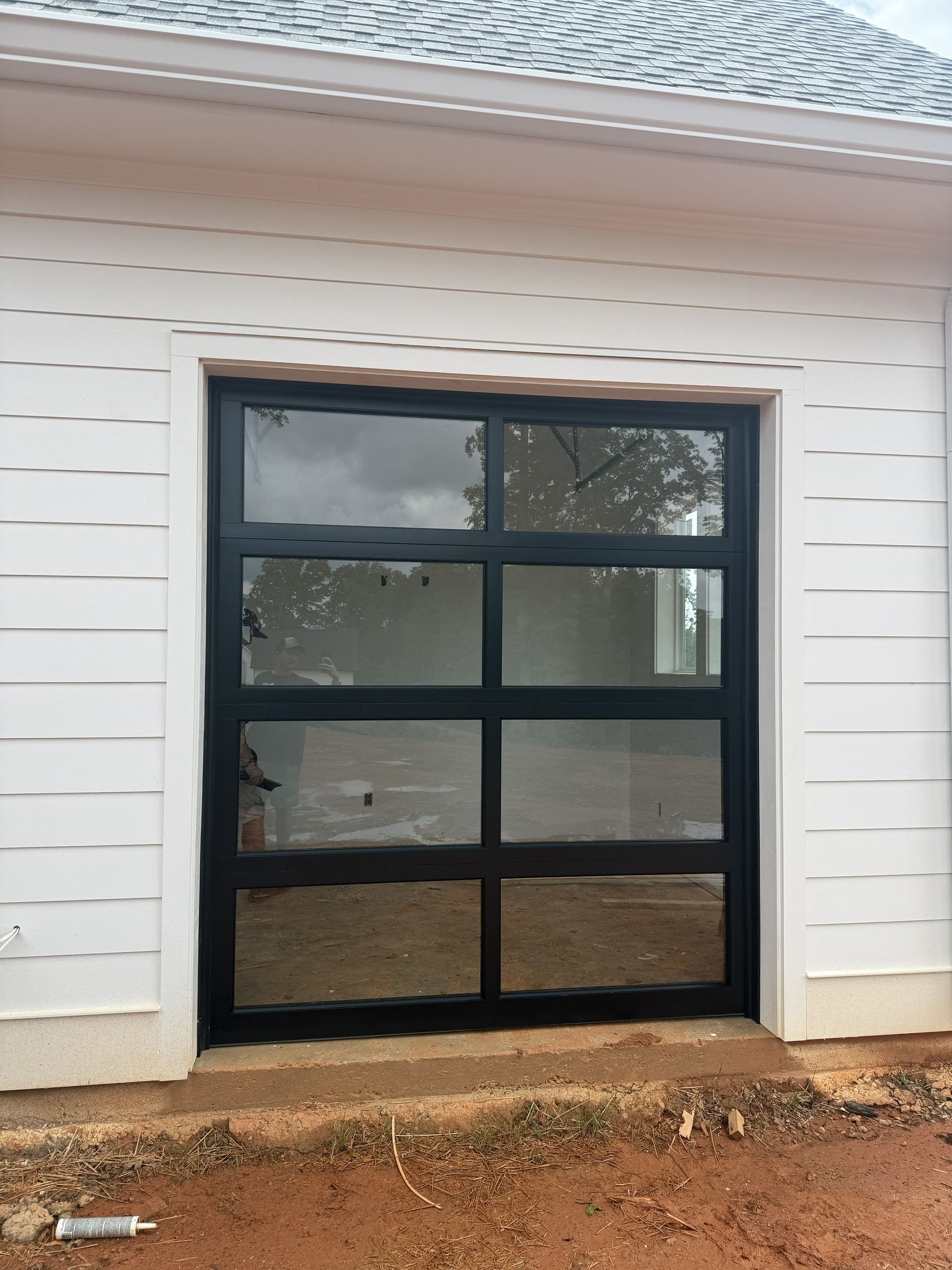 Black-framed, glass garage door in a white building. Ground is dirt.