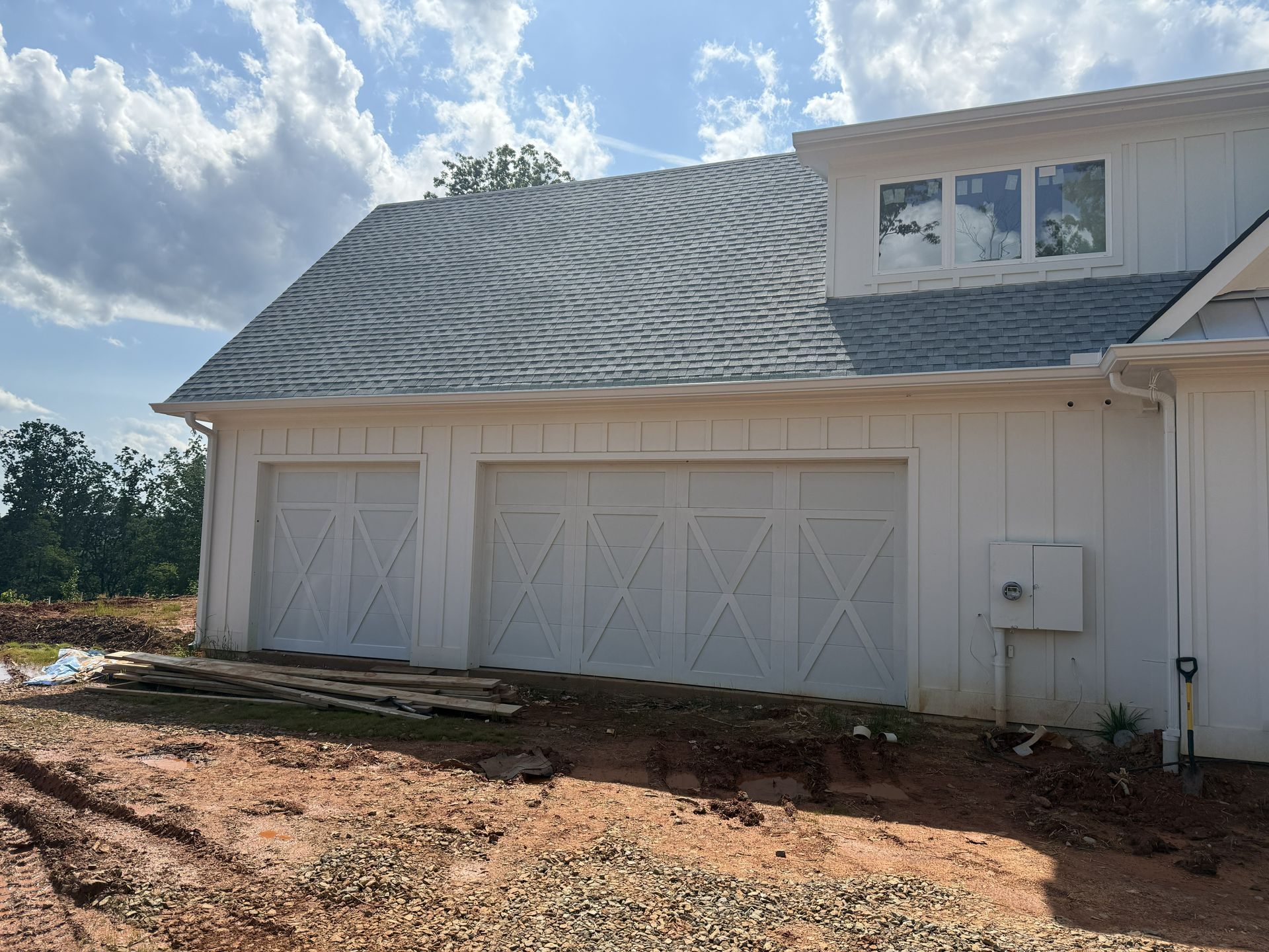 White garage with two doors and a gray roof under a partly cloudy sky.
