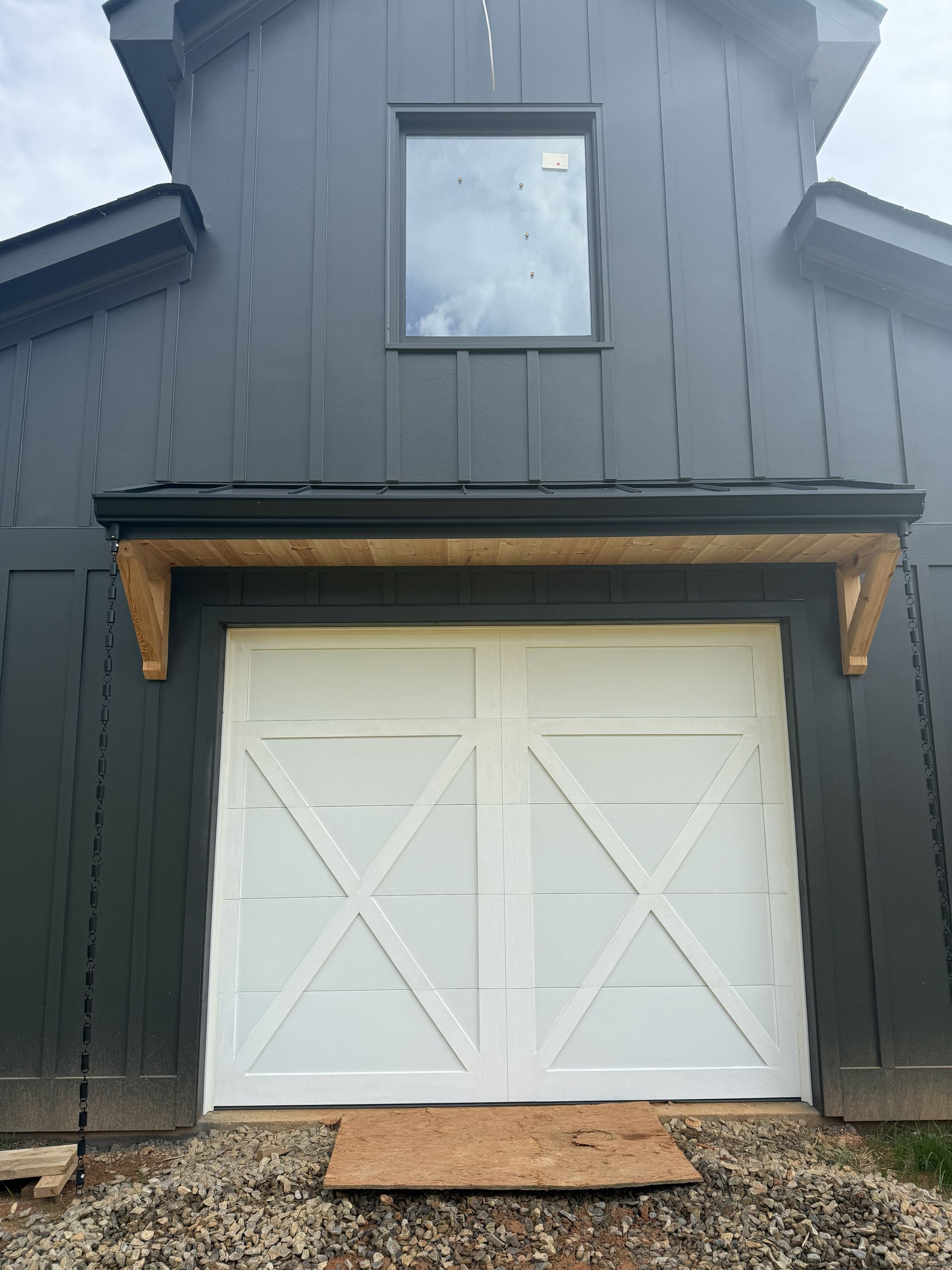 White garage doors with X-shaped accents, under a dark gray barn-style building with a small window.