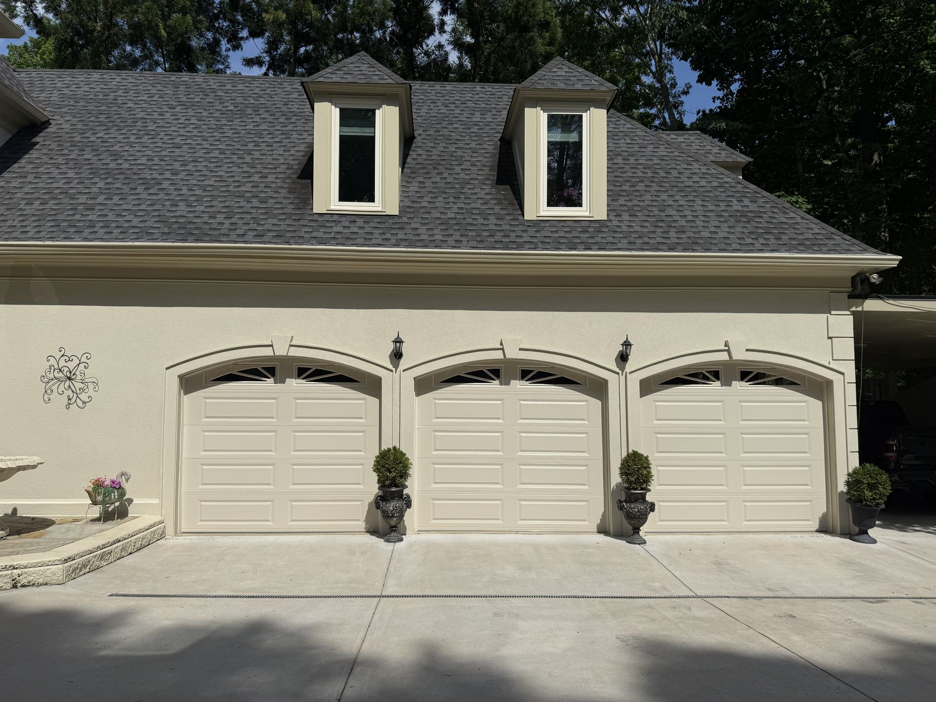 Three-car garage with cream-colored doors and dormer windows on a house with a gray roof.