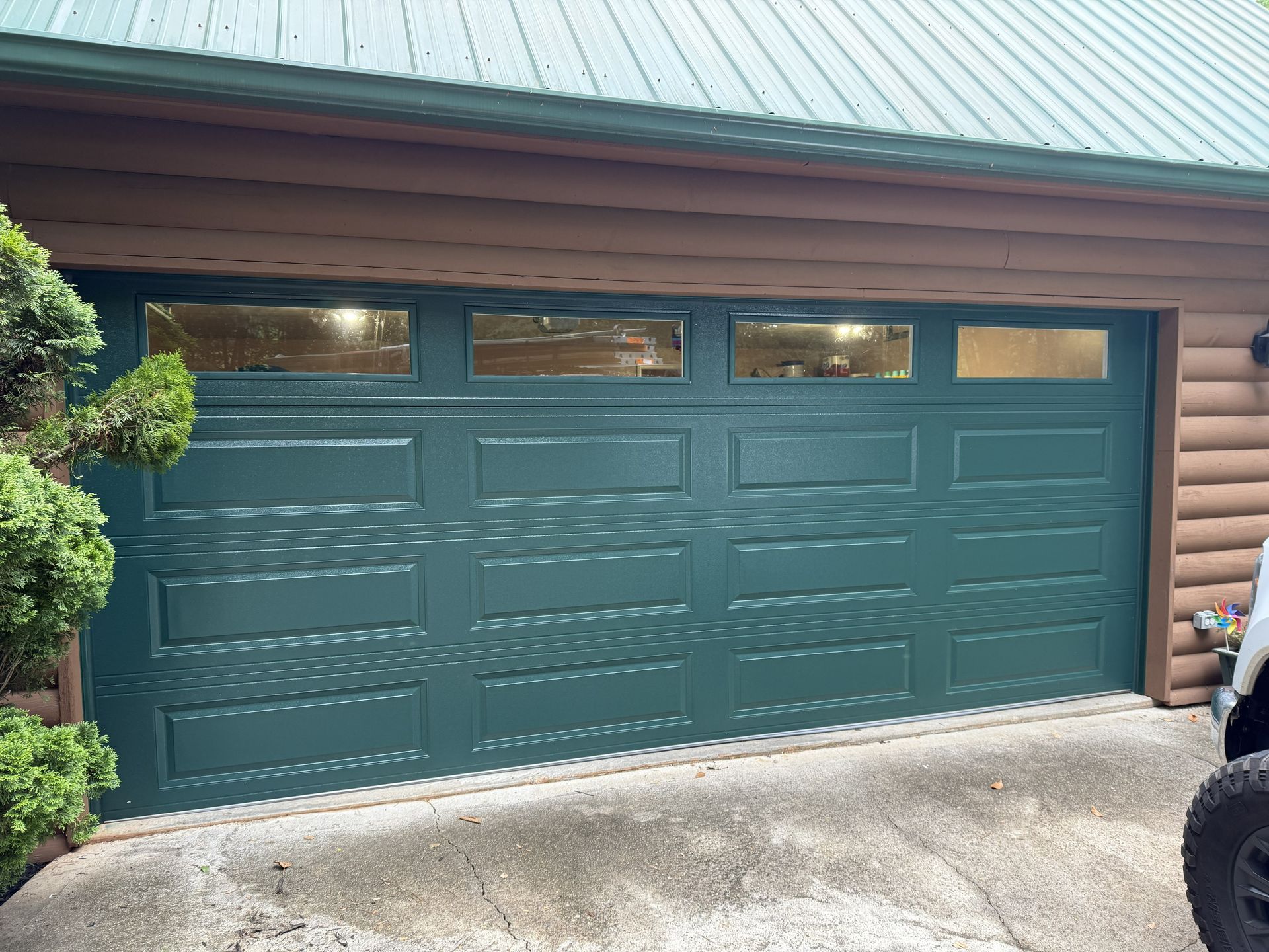 Green garage door with windows, set in a log cabin style building.