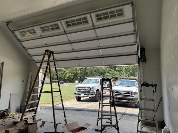 Garage door partially open; two ladders inside; two white trucks outside.