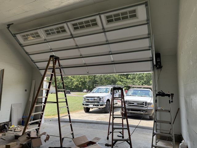 Garage door partially open; two trucks parked outside. Ladders inside, construction in progress.