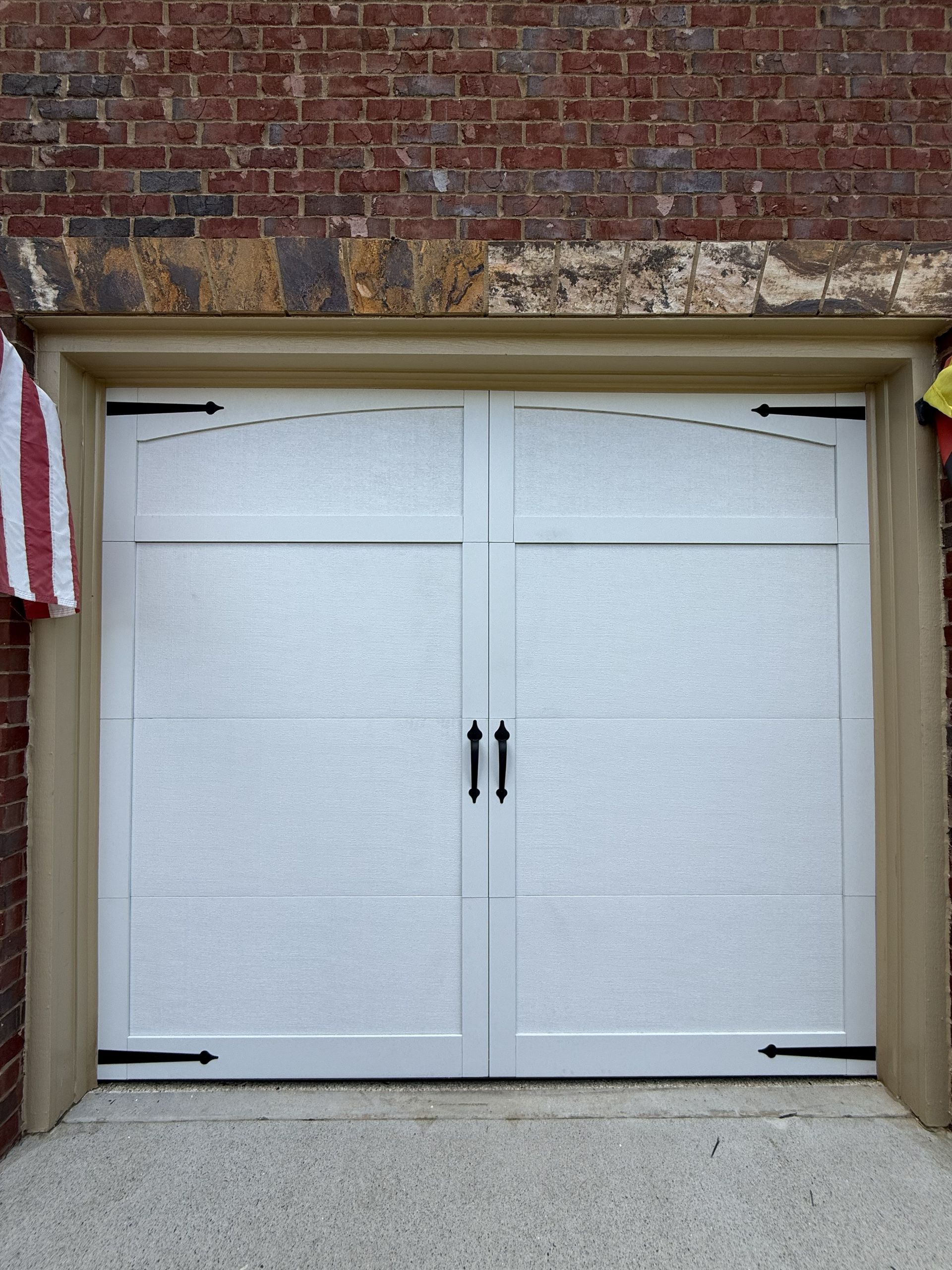 White garage door with arched top, black hardware, set in a brick wall.